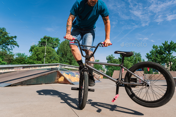 A skilled urban tattooed bmx rider is practicing tricks in a skate